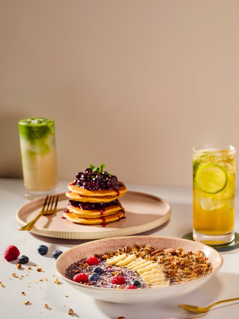 Acai bowl with granola and berries beside pancakes and iced drinks